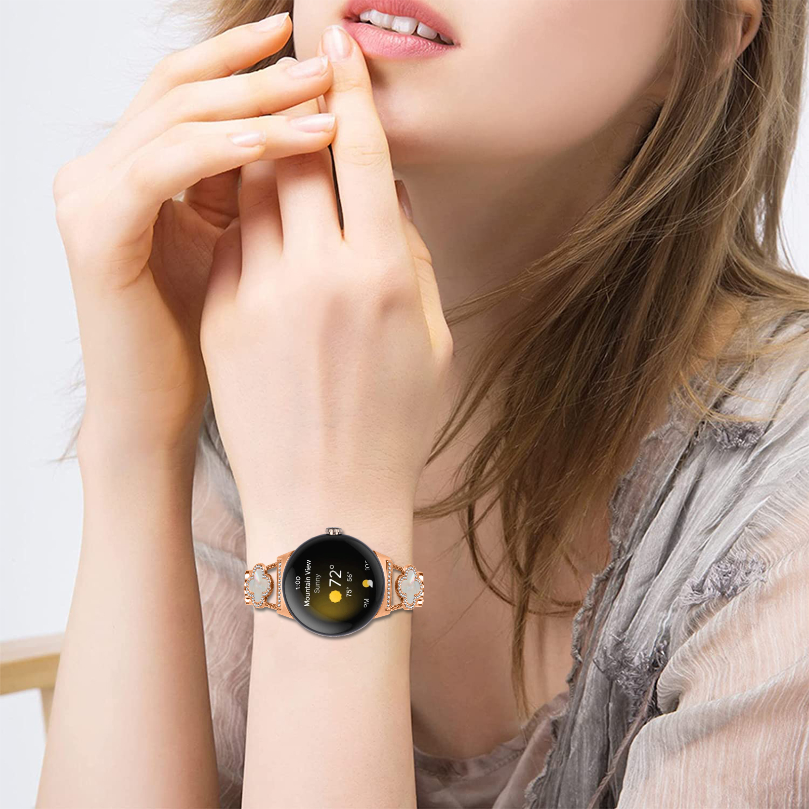 Handgelenk einer Frau mit roségoldener Uhr. Es hat ein Kleeblattband und das Zifferblatt zeigt Wetter.