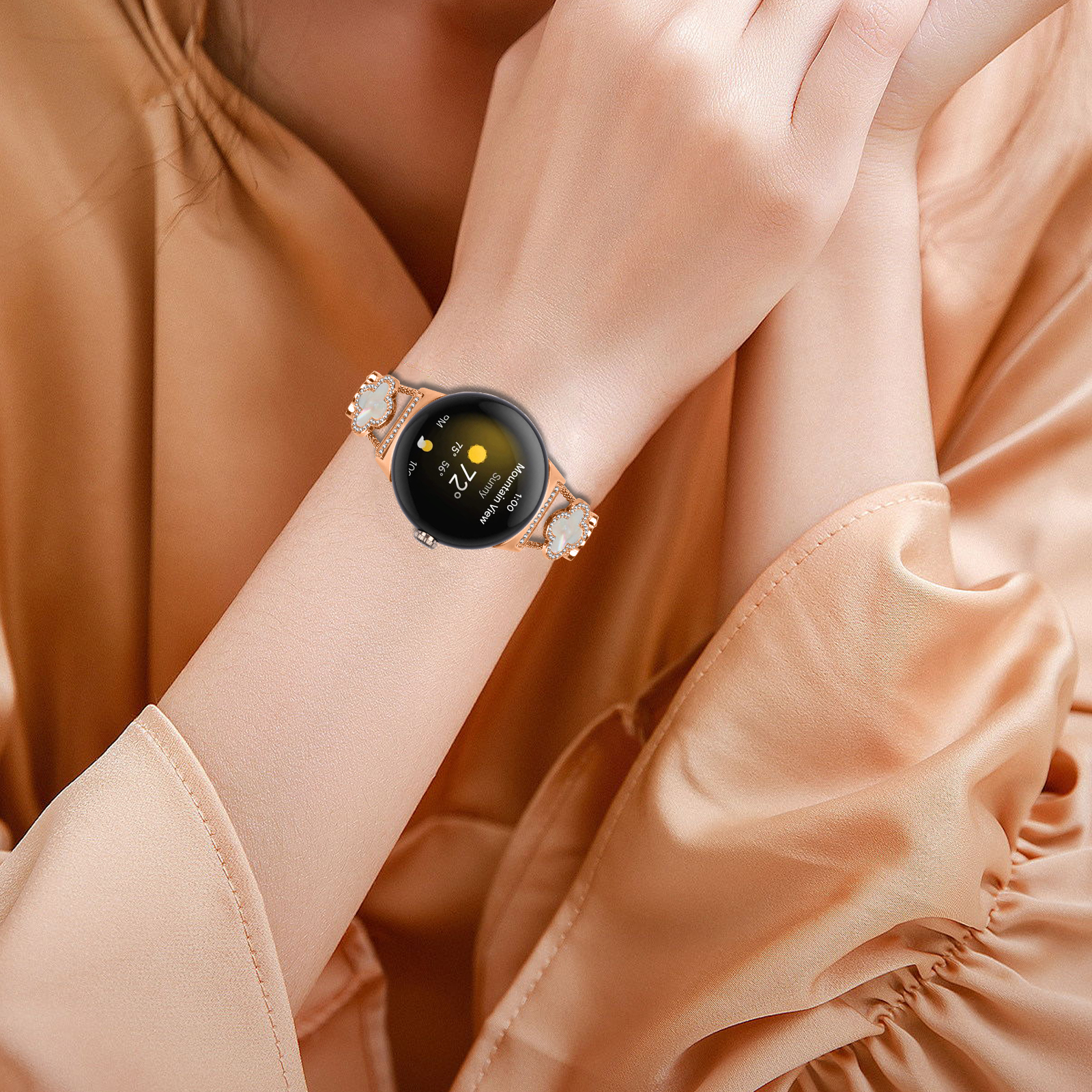 Handgelenk einer Frau mit roségoldener Smartwatch und Band, verziert mit Kleeblatt-Kristallen.