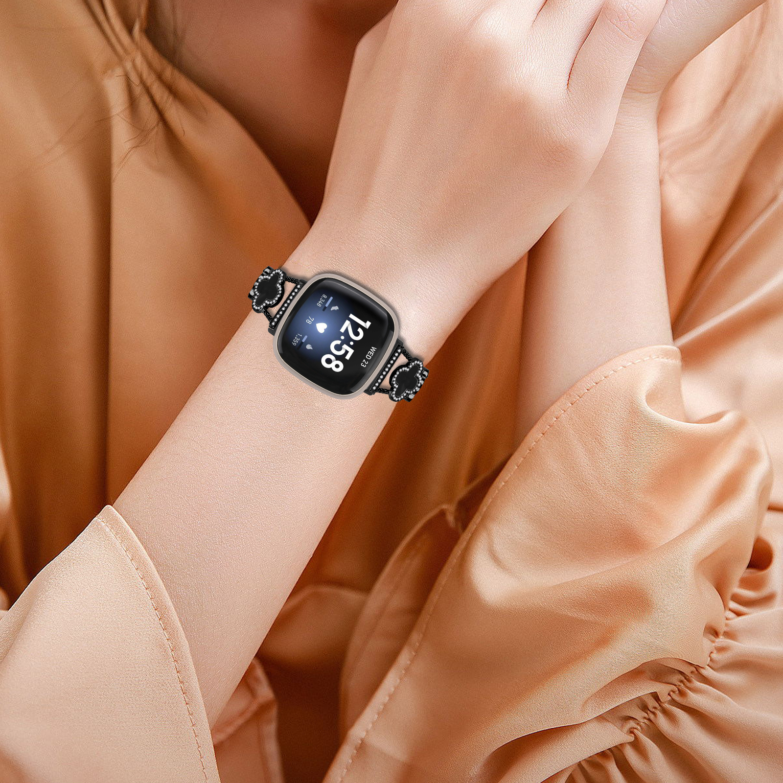 Handgelenk mit schwarzer Smartwatch. Die Uhr hat ein schwarzes Blumenarmband und zeigt Zeit und Datum.