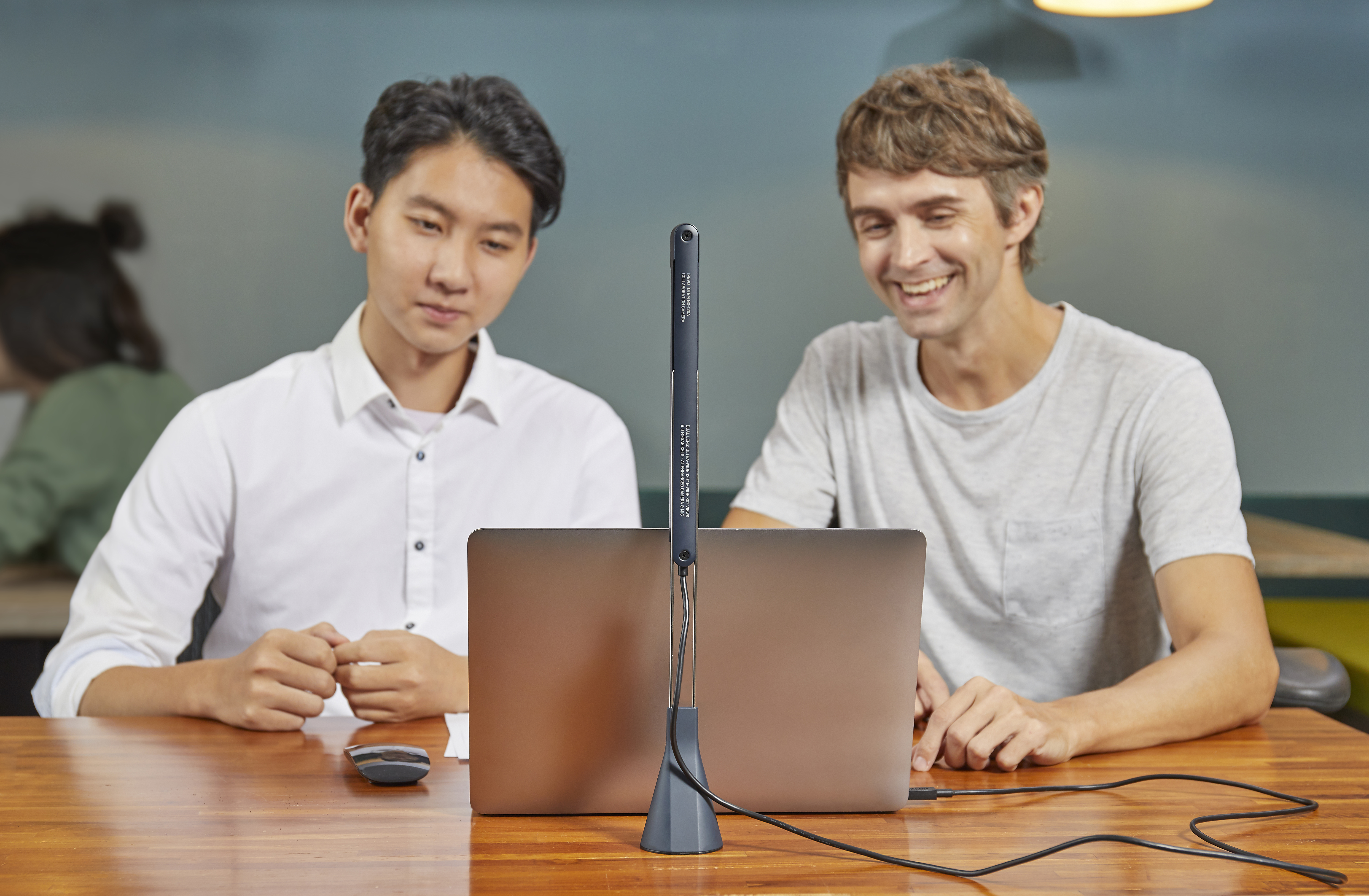 Deux hommes regardant un ordinateur portable. Une lumière est fixée à l'écran. Table en bois.