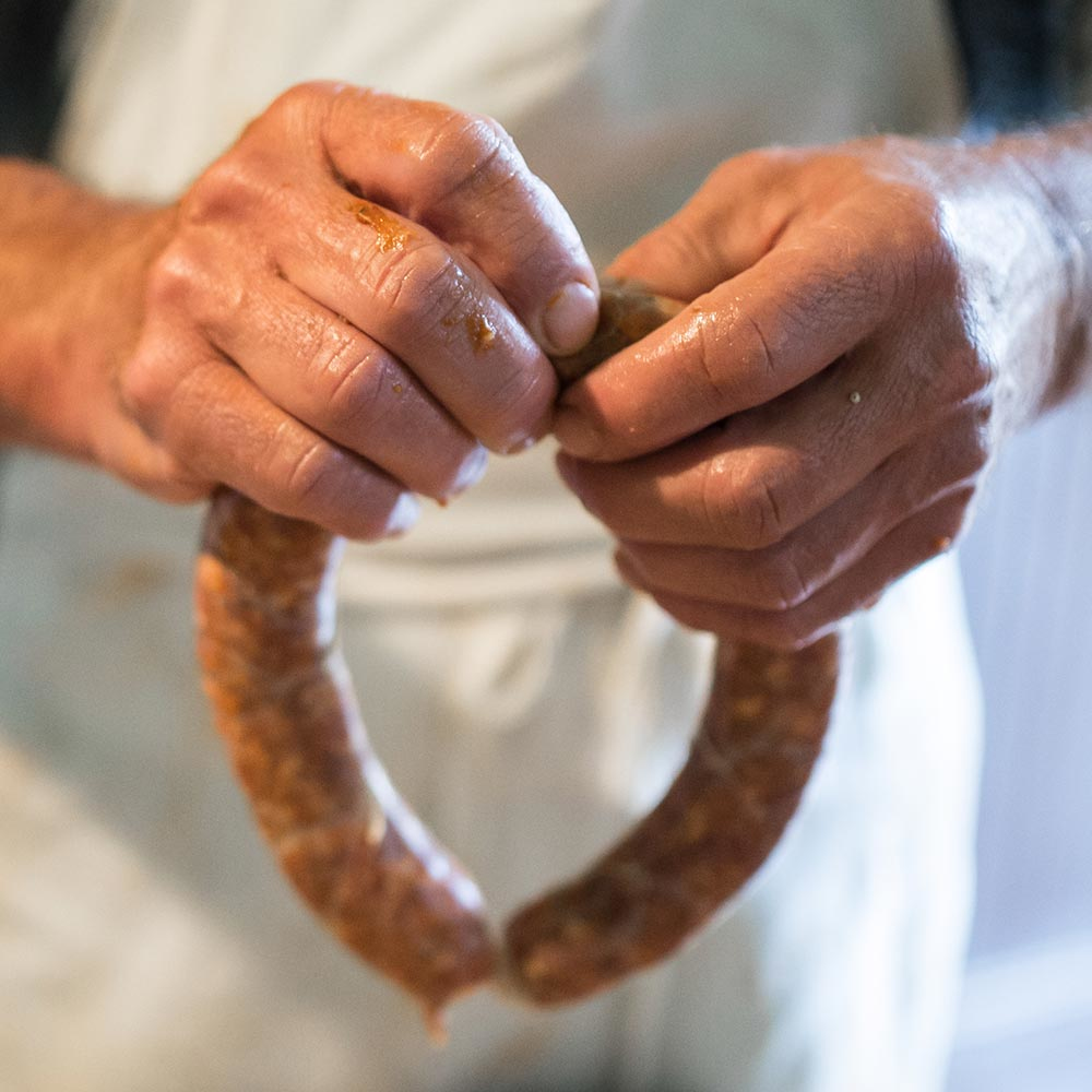 Dłonie trzymające pierścień kiełbasy, zbliżenie. Kiełbasa jest brązowa i ma widoczną teksturę.