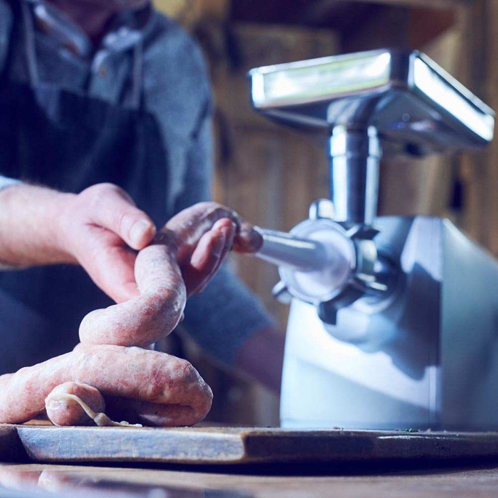 Osoba robiąca kiełbasę za pomocą maszynki do mięsa, kiełbasa na drewnianej desce, drewniane tło.