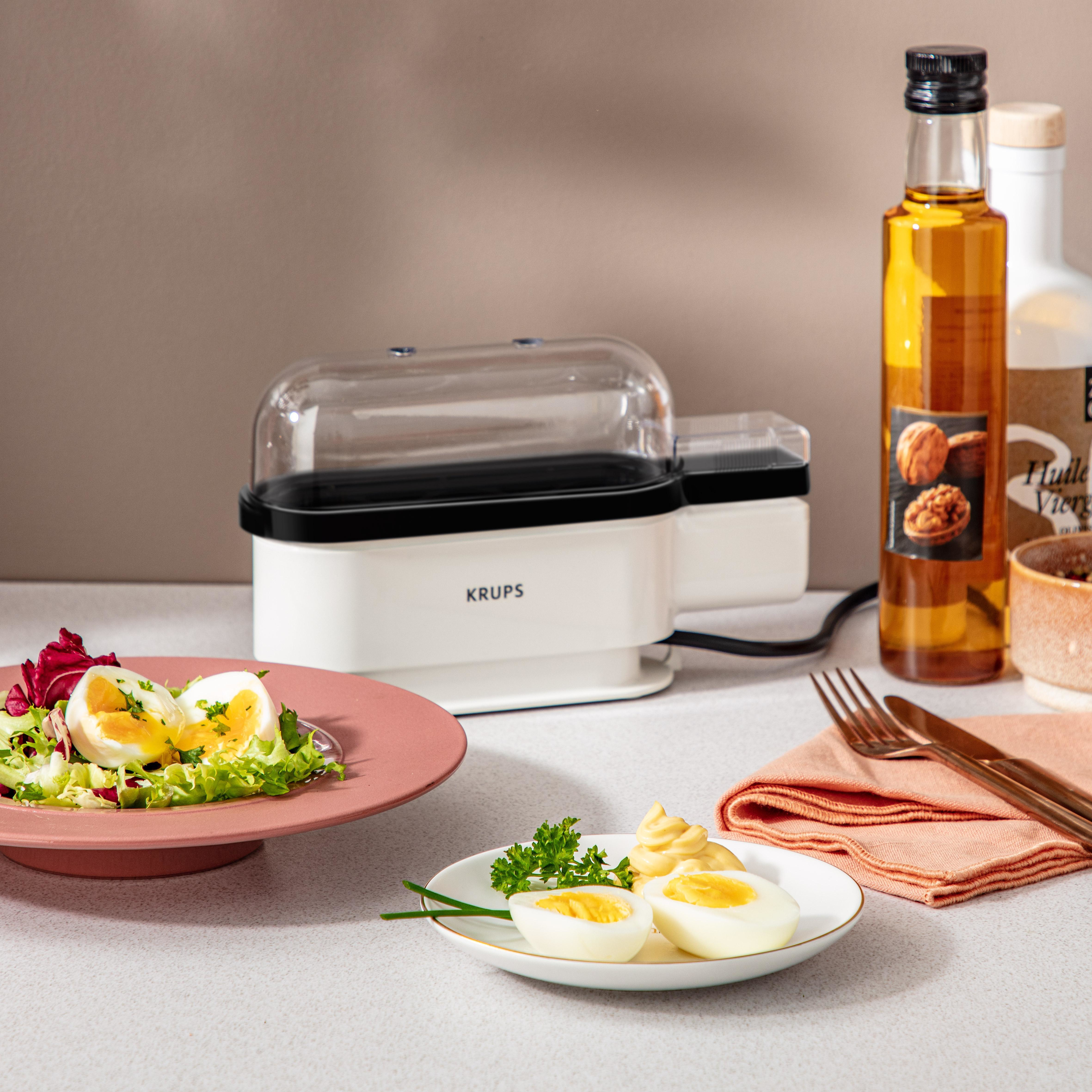 Biało-czarne urządzenie do gotowania jajek z jajkami i składnikami, takimi jak olej i pietruszka na stole.