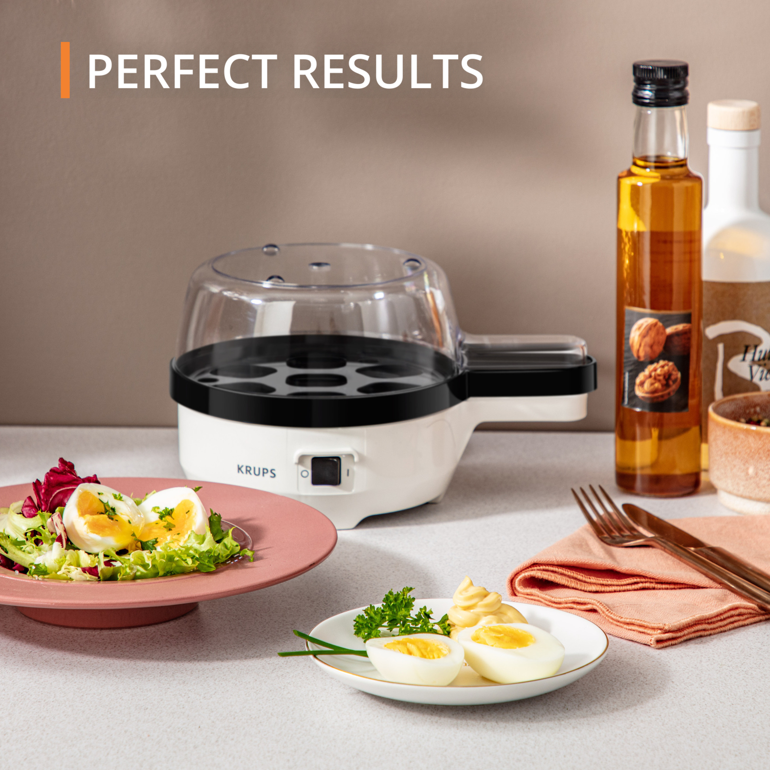Gotowacz do jajek z ugotowanymi jajkami, butelkami z olejem i sałatką na różowym talerzu.