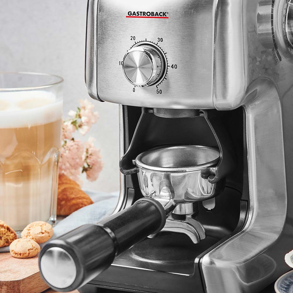Macchina per espresso con portafiltro in uso. Tazza di latte e pasticcini sul lato sinistro.