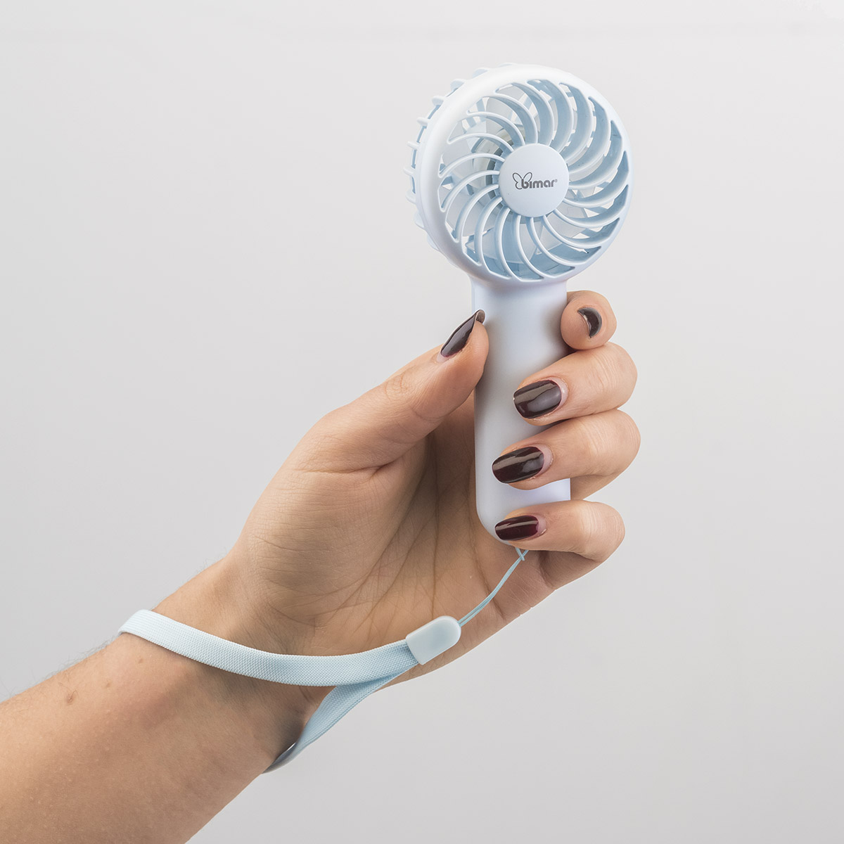 Mano che tiene un piccolo ventilatore personale bianco e blu. Sfondo chiaro.