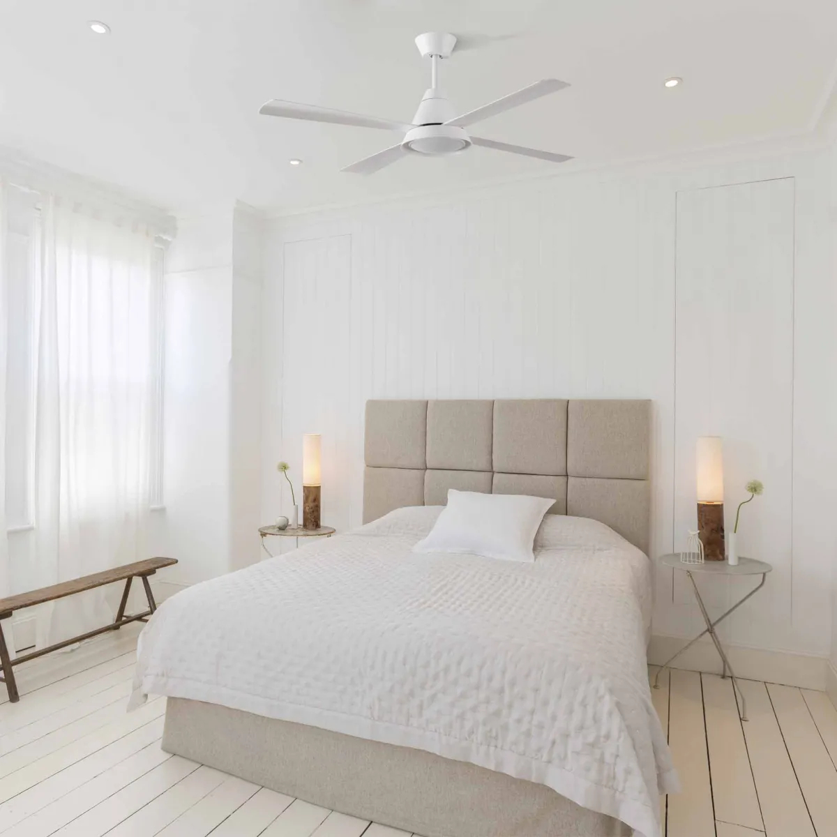 A bright white bedroom with a bed, side tables, and a ceiling fan. White walls and floor.
