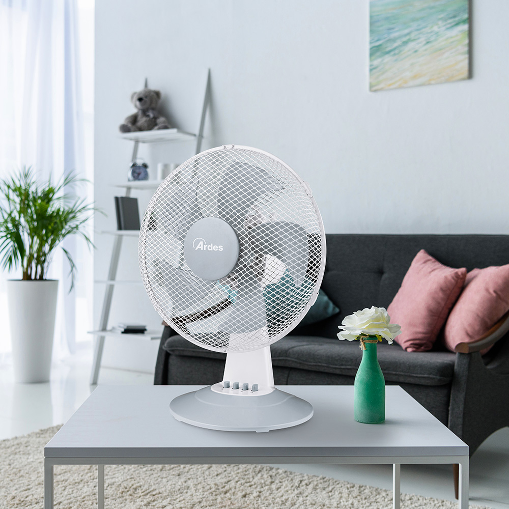 Witte tafelventilator op een tafel. Een bank en een plant op de achtergrond.