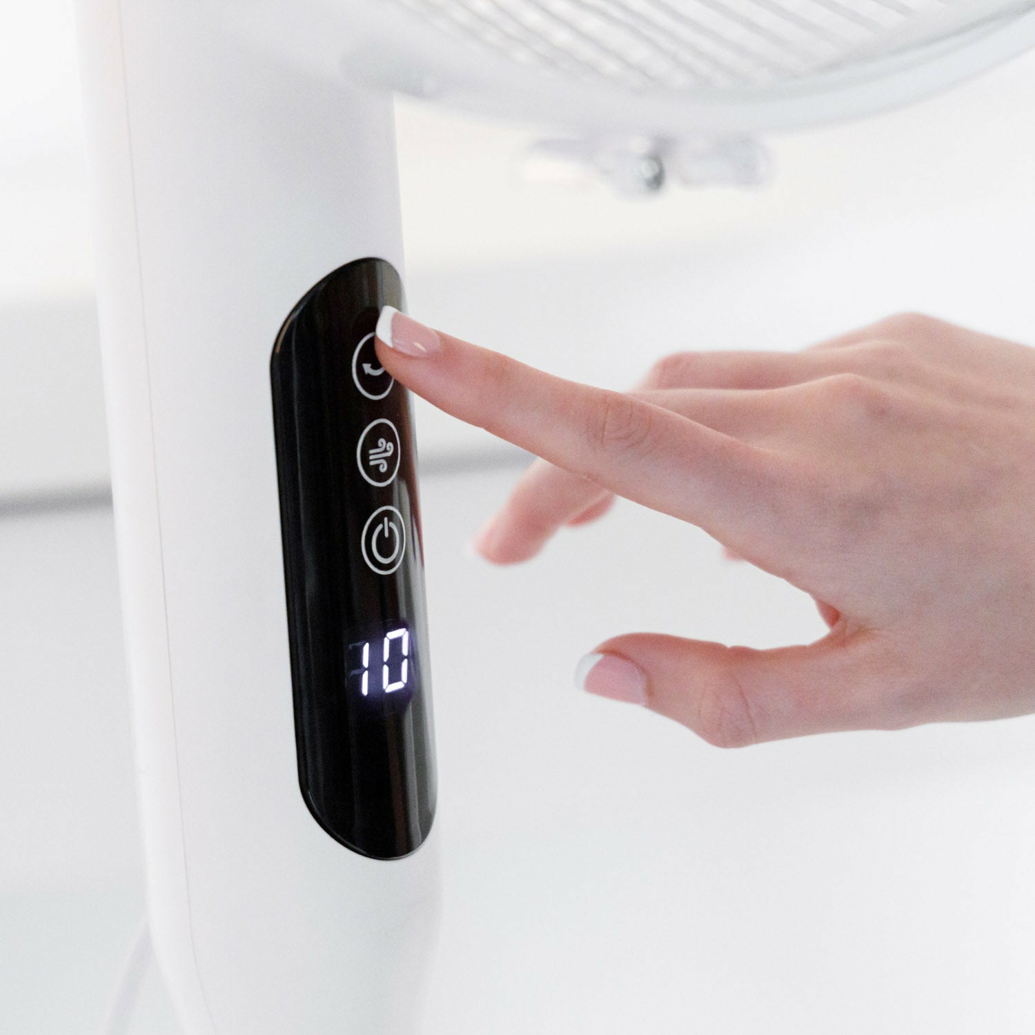 Una mano presiona un botón en un ventilador blanco. El ventilador tiene una pantalla digital que muestra el número 10.