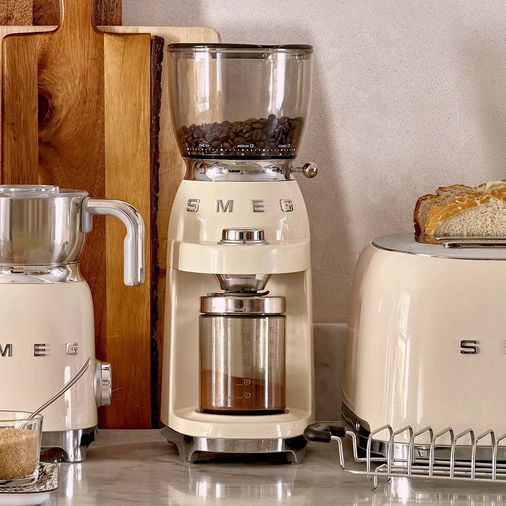 Escena de cocina con molinillo de café SMEG beige, tostadora y espumador de leche.