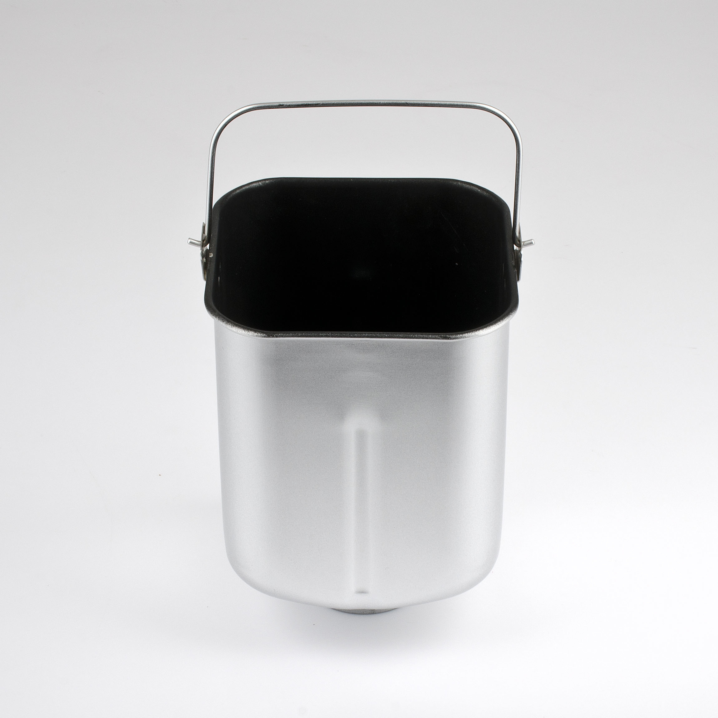 Błyszczący srebrny pojemnik do wypieku chleba z czarnym wnętrzem i srebrnym uchwytem. Jest na białej powierzchni.