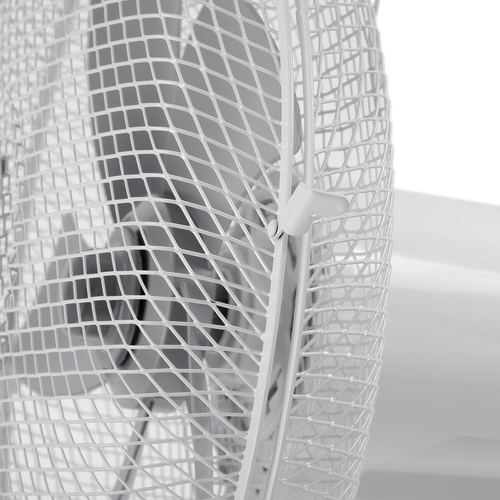 Primer plano de la rejilla protectora de un ventilador blanco. Está hecha de un patrón entrecruzado con un marco blanco.
