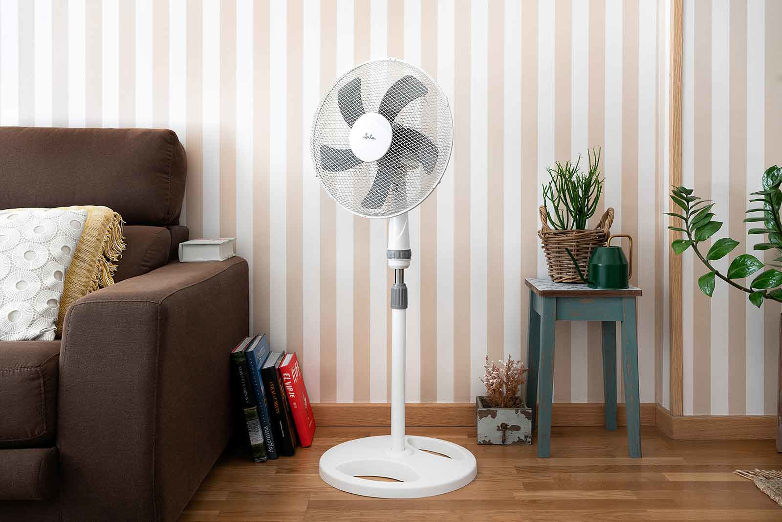 Un ventilador de pie blanco en una sala de estar con un sofá marrón.