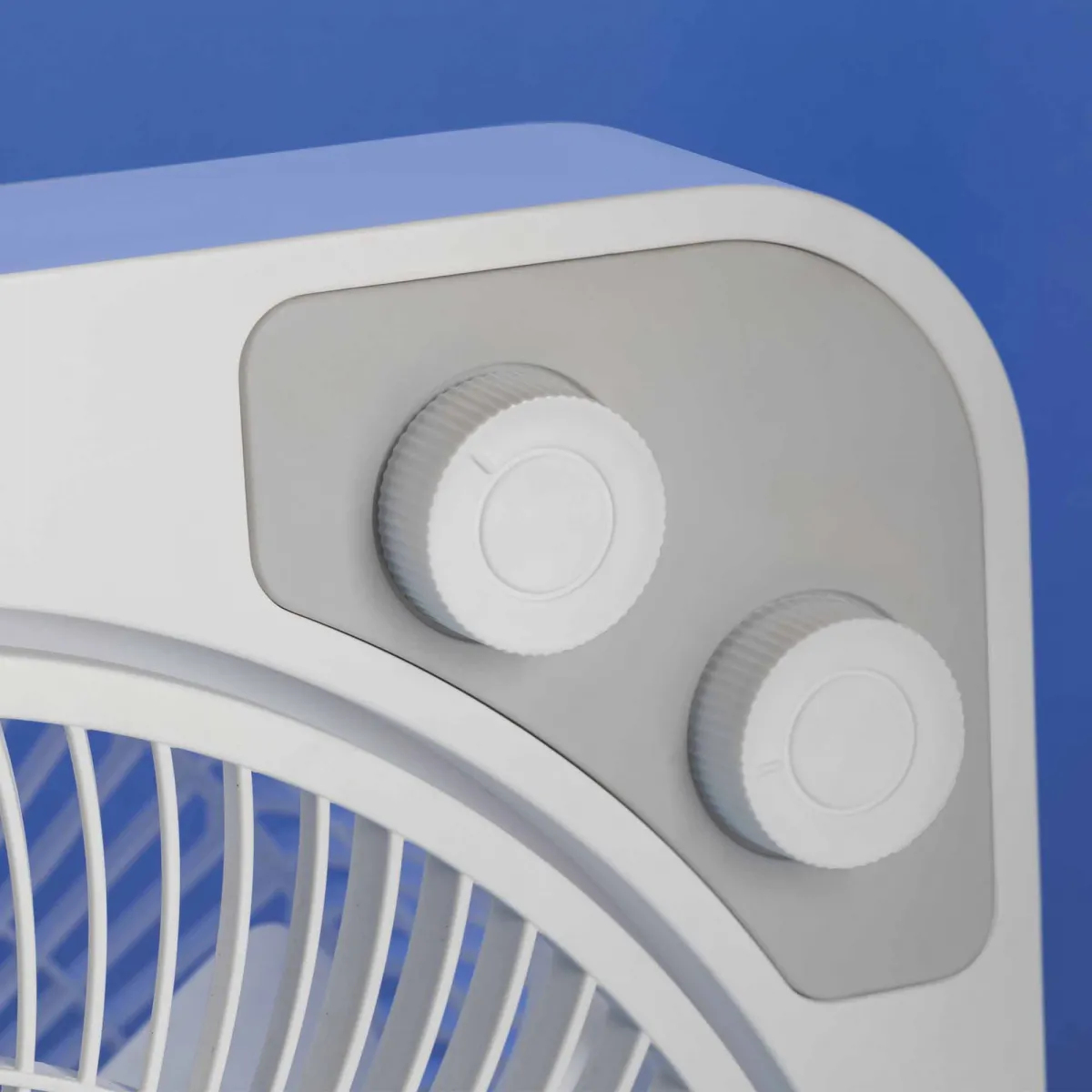 Primer plano de un ventilador blanco y gris con dos perillas de control.