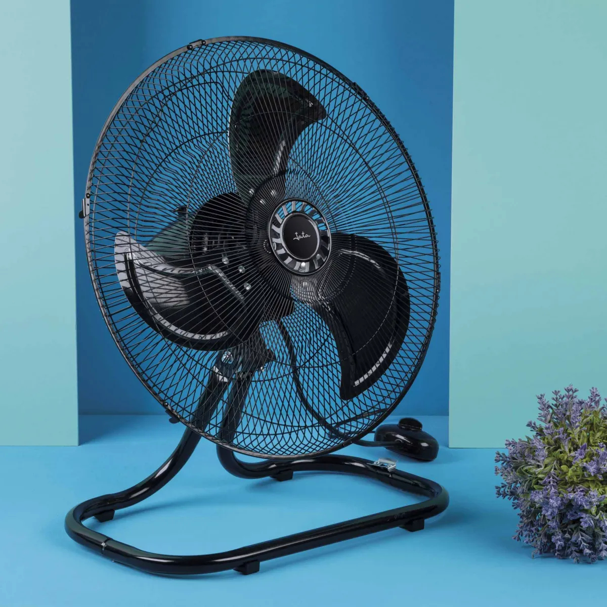 Un ventilador negro con base curva sobre un fondo azul. Es una configuración de estudio.