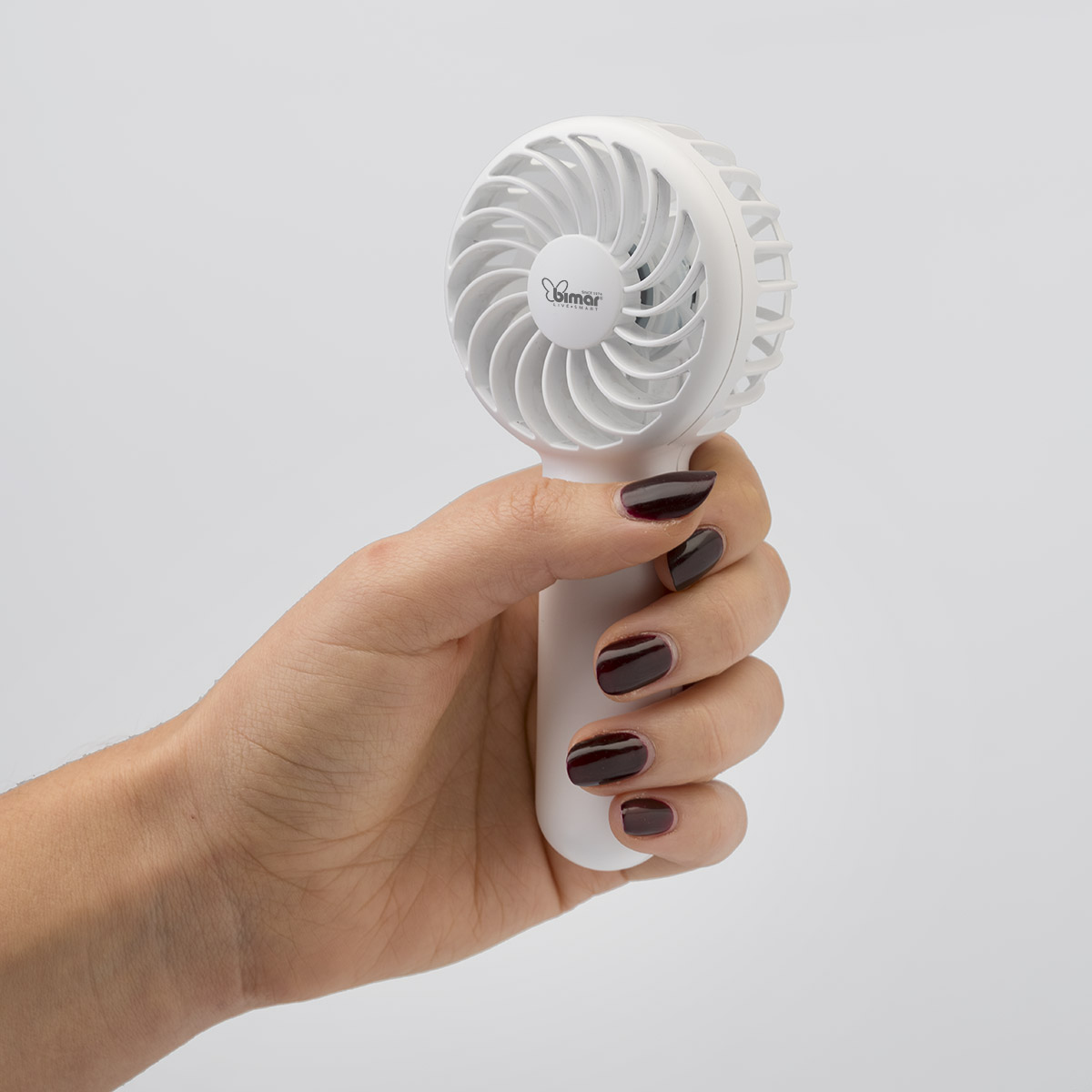 Een witte Bimar handventilator in een hand met donkerrode nagellak.