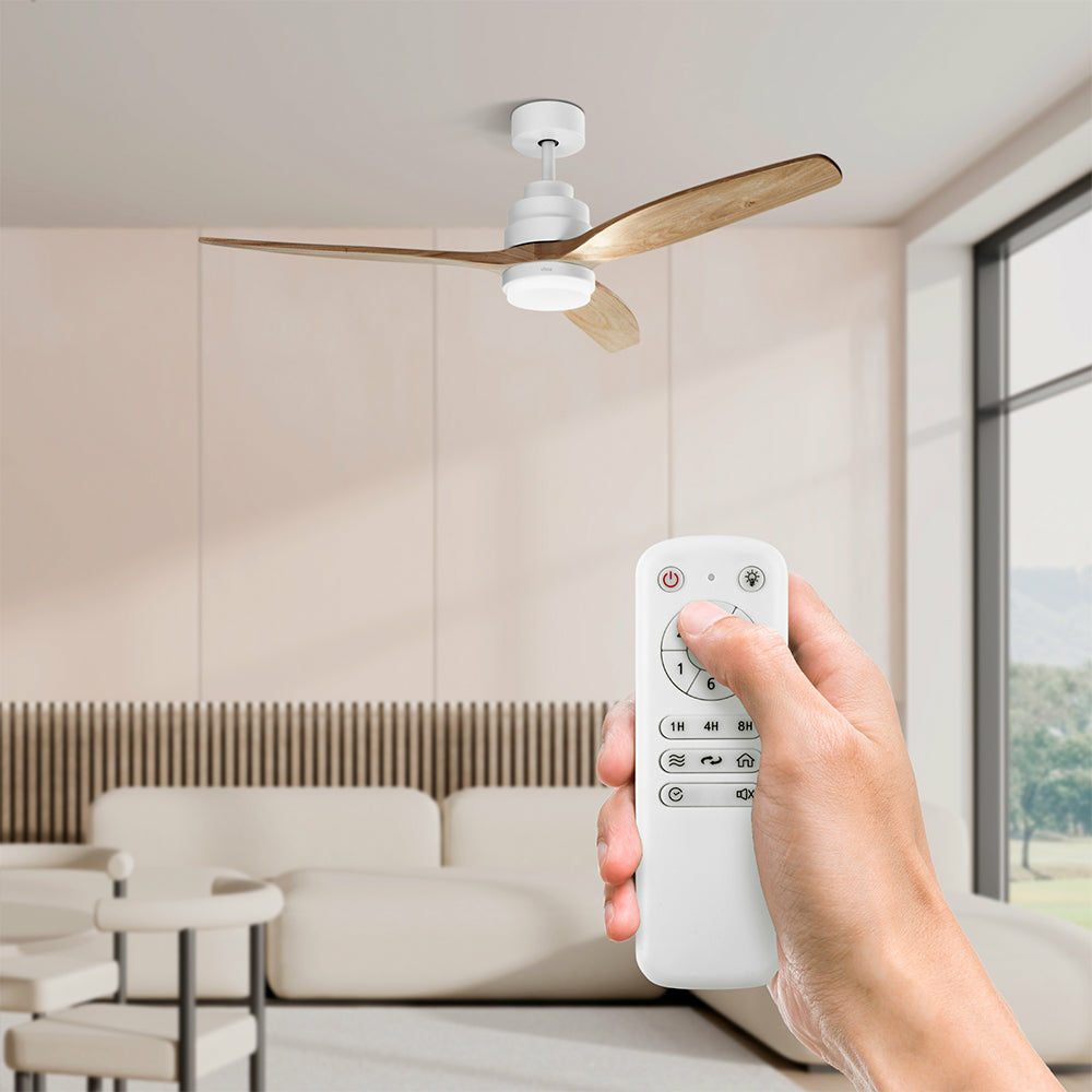 Persona sosteniendo control remoto blanco para ventilador de techo. Ventilador con aspas de madera, en habitación.
