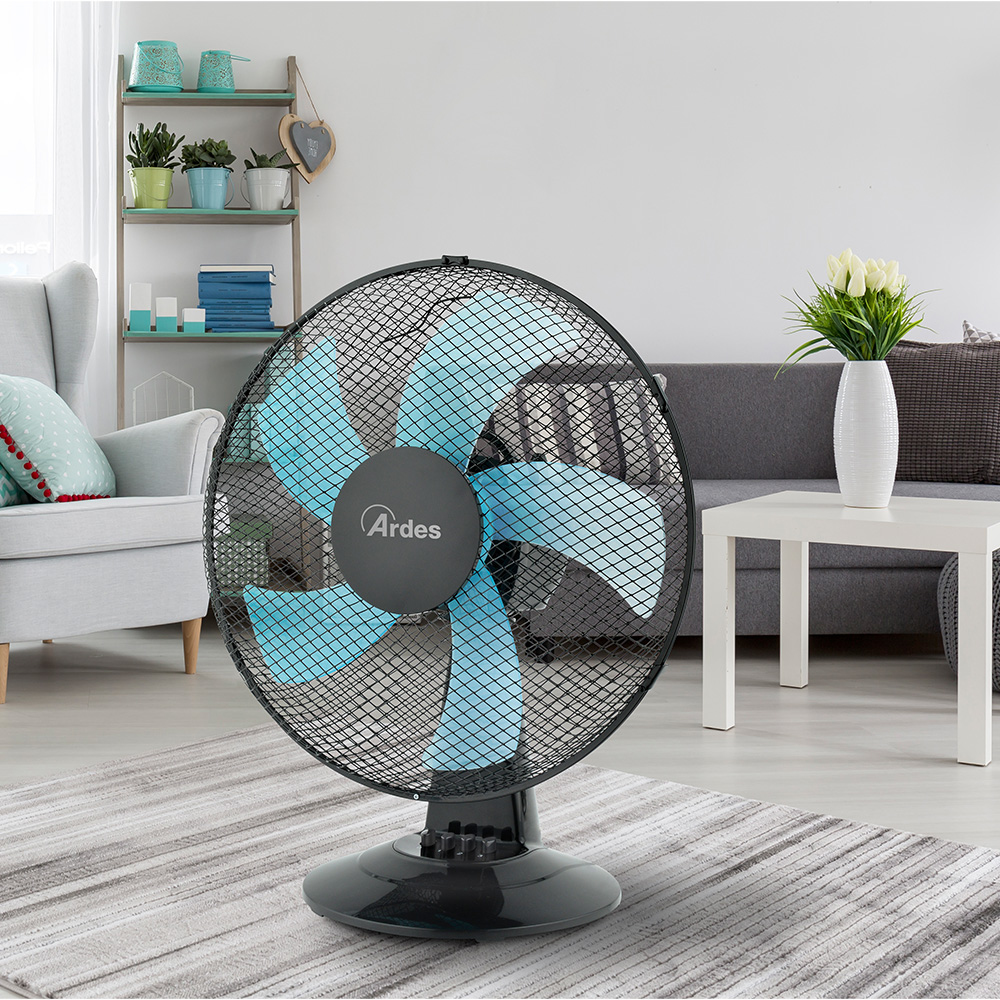 Wentylator Ardes z niebieskimi łopatkami, czarną kratką, na podłodze w salonie z meblami w tle.