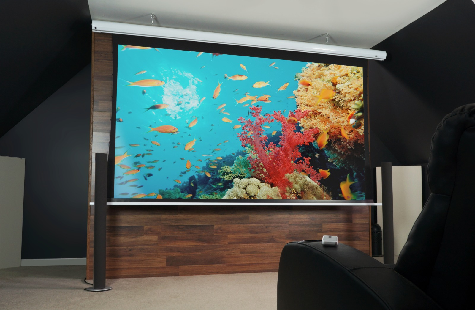Heimkino-Setup mit großem Bildschirm, der eine Unterwasserszene mit Fischen zeigt. Ein schwarzer Relaxsessel im Vordergrund.