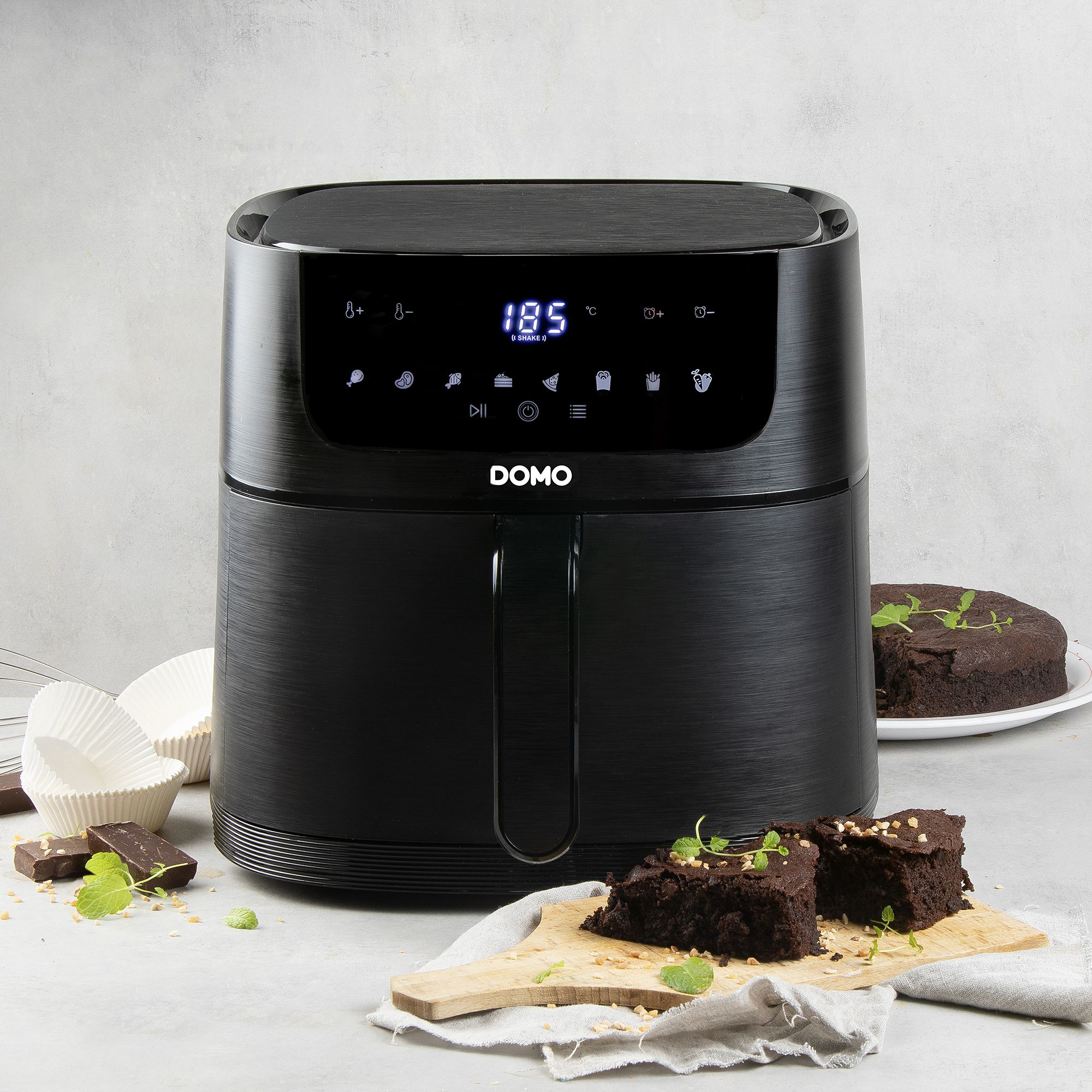 Schwarze Heißluftfritteuse mit LED-Anzeige, Kuchen und Brownies auf heller Oberfläche.