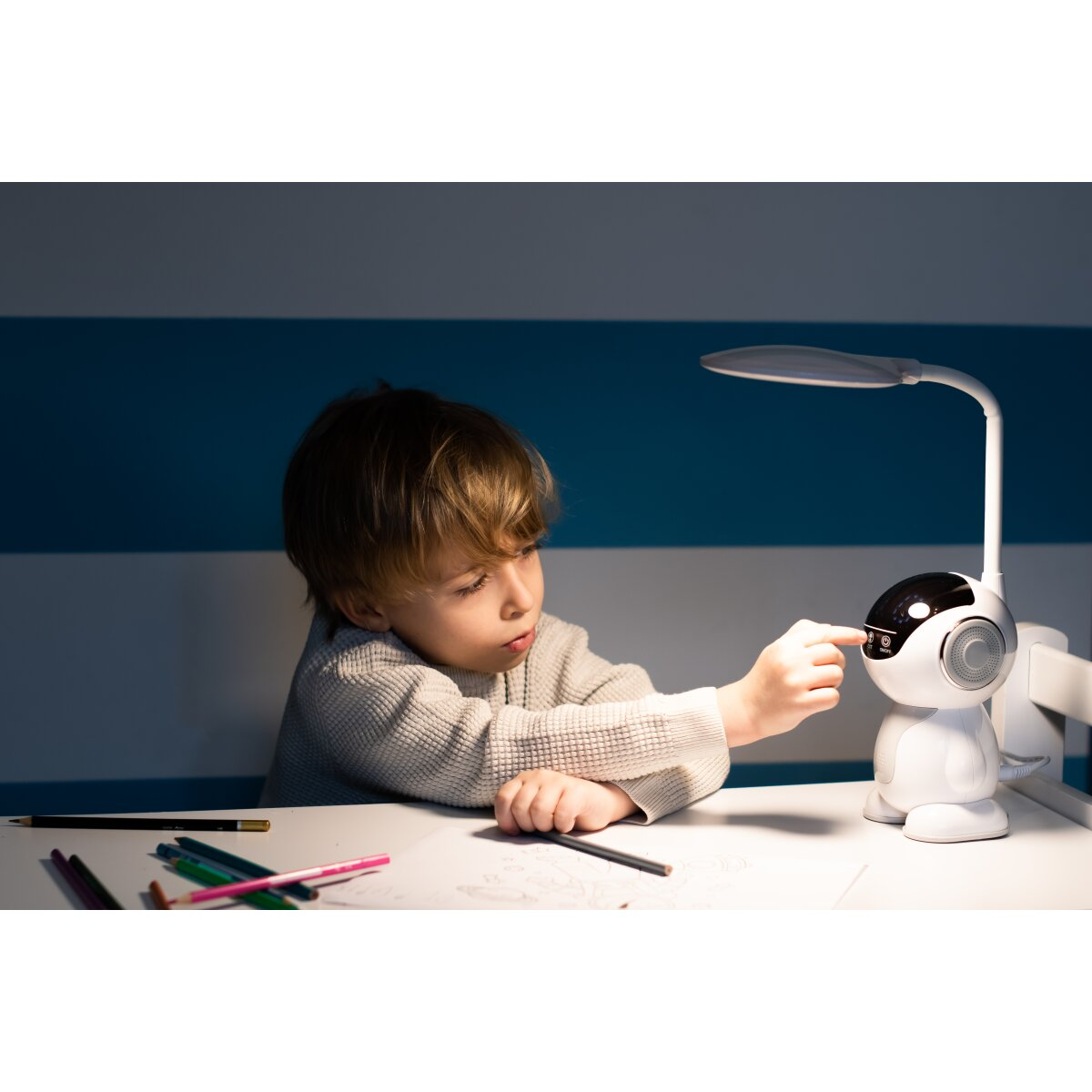 Un bambino sta toccando una lampada da scrivania robot. La lampada ha uno schermo e una luce.