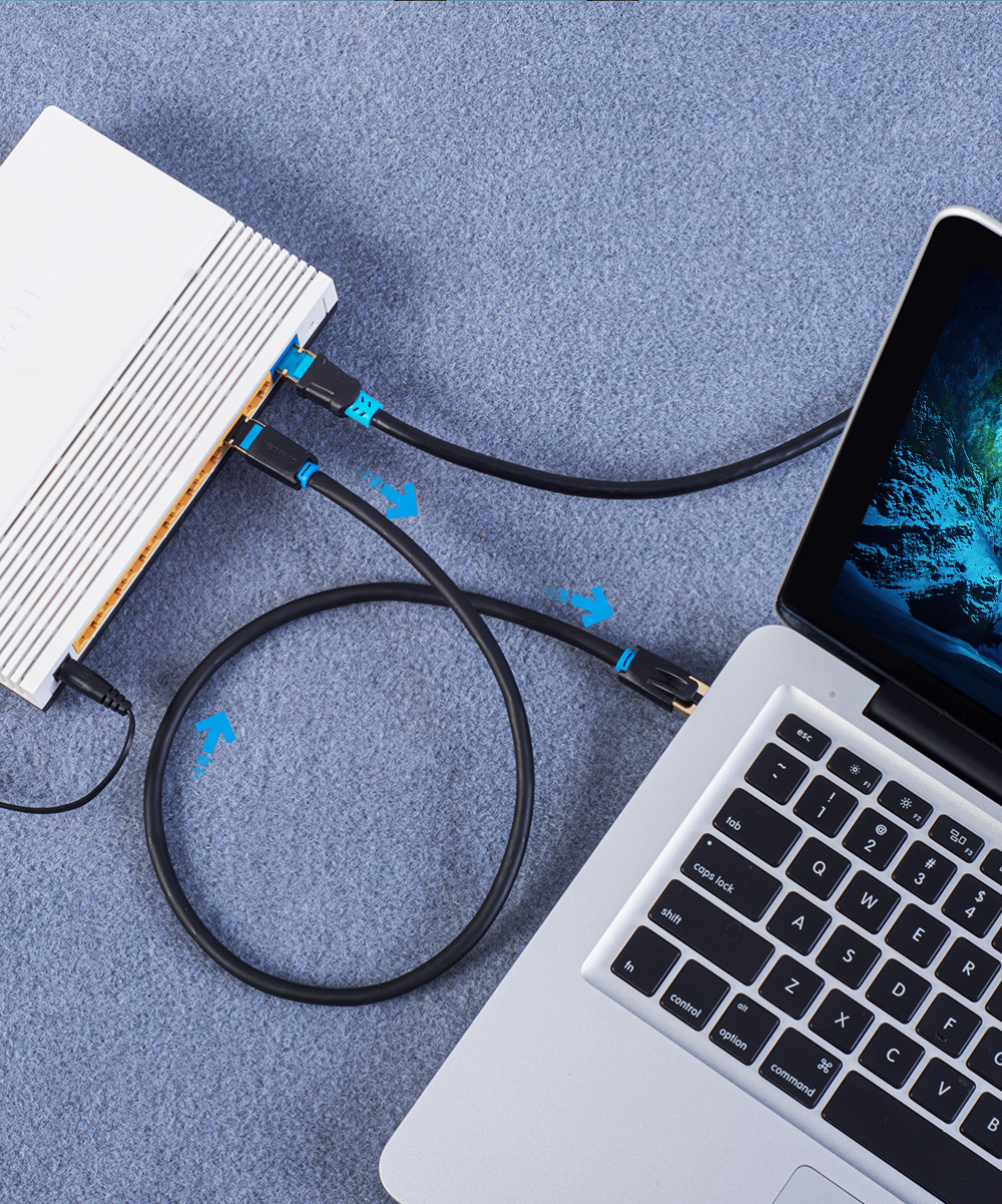 Laptop podłączony do białego routera. Czarne kable z niebieskimi końcami łączą router z laptopem.