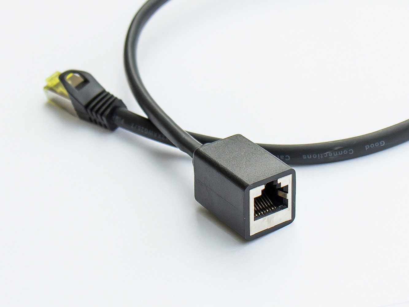 Czarny kabel sieciowy z czarnym złączem i żeńskim portem. Białe tło.