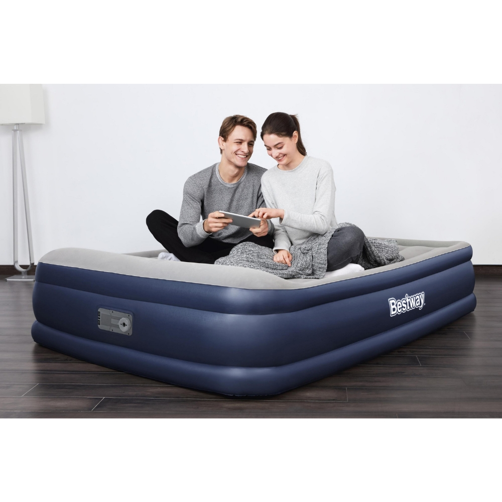 Koppel op een donkerblauw luchtmatras, een tablet gebruikend. Lichte kamer met een staande lamp.
