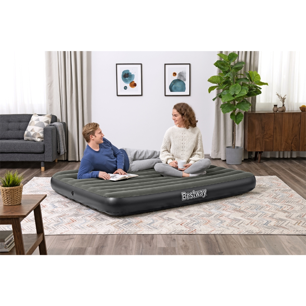 Koppel zit binnen op een grijs opblaasbaar matras. De achtergrond bevat meubels.