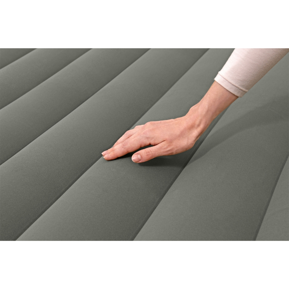 La main d'une personne touche doucement un matelas gonflable gris et strié. La personne porte une chemise à manches longues.