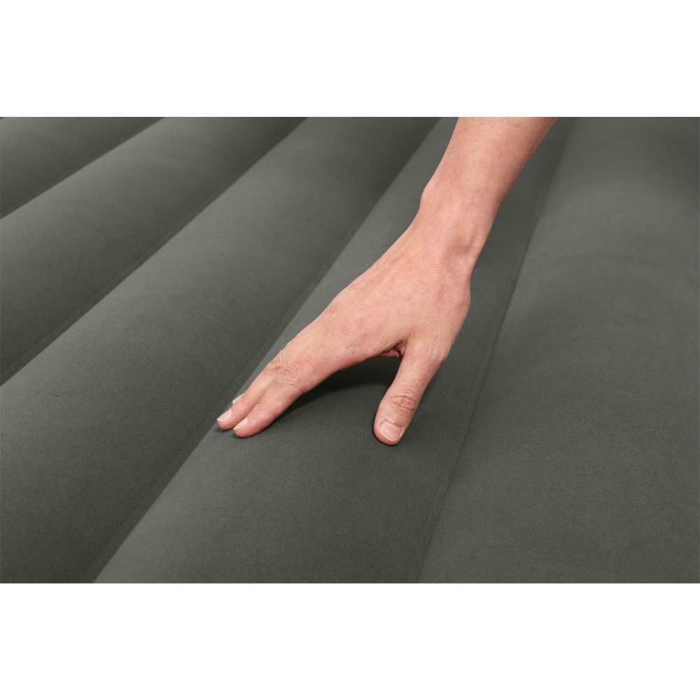 Une main touche doucement un matelas gonflable gris et strié. La surface est lisse.