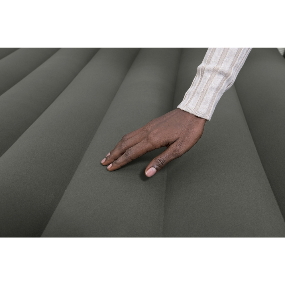 Une main touche un matelas gonflable gris foncé. Le fond est un mur blanc.