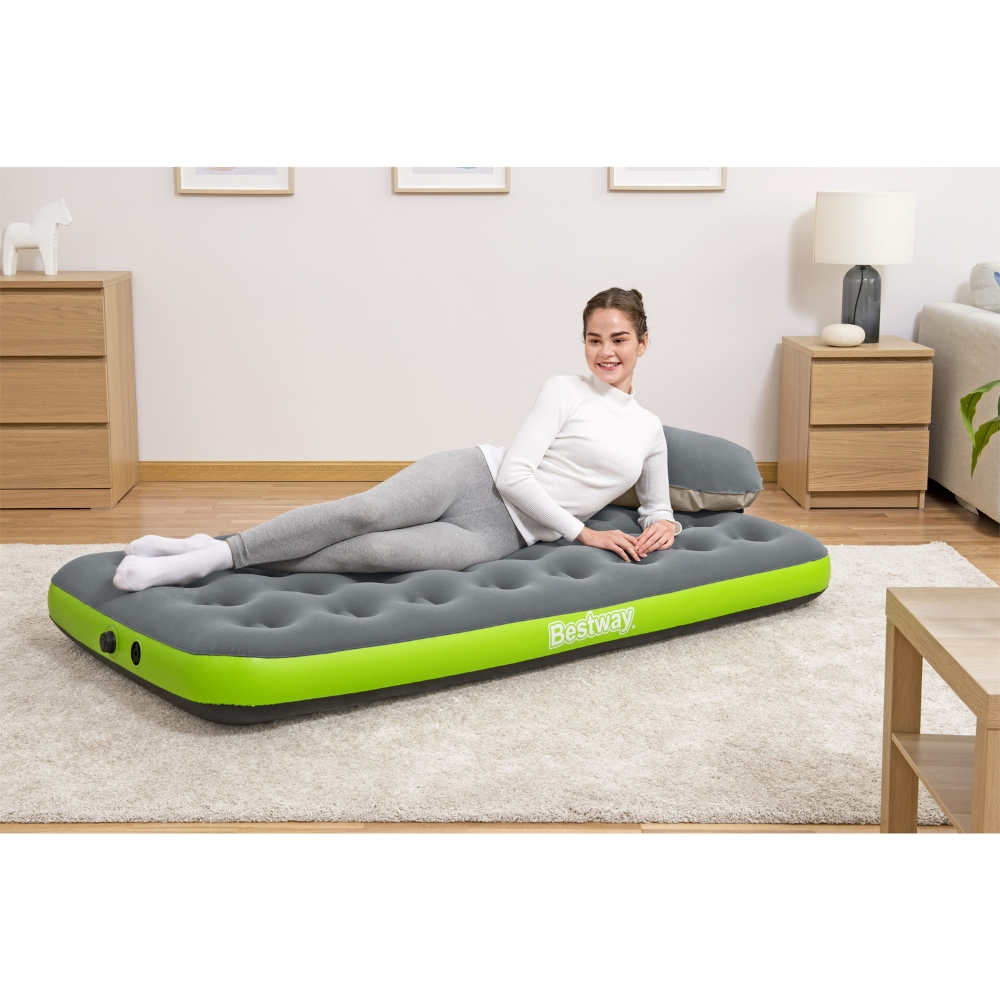 Een vrouw ligt op een grijze en groene opblaasbare matras. Ze glimlacht. Er is een Bestway-logo.