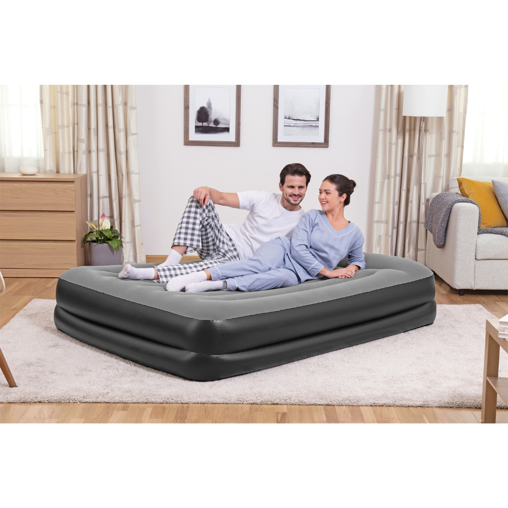Couple sur un matelas gonflable dans une pièce. Ils sourient et la pièce a des meubles et des rideaux.