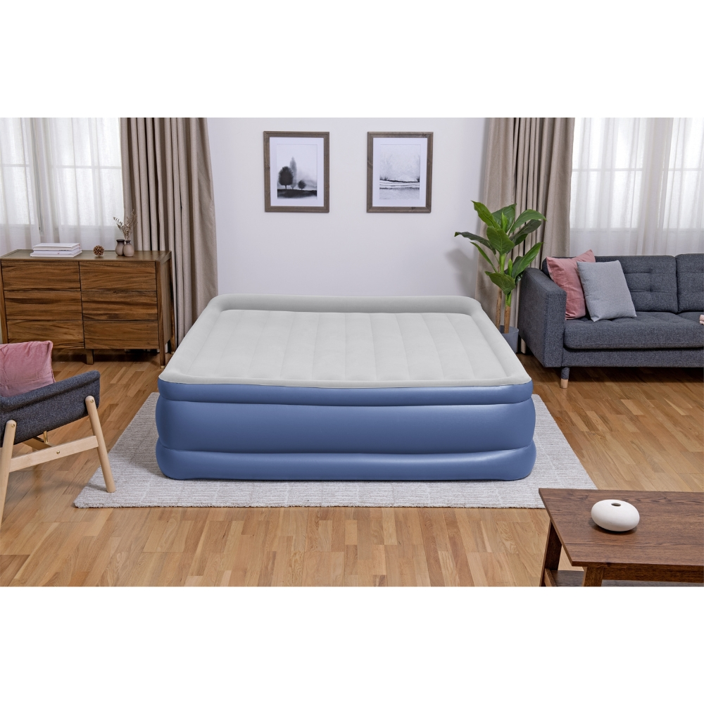 Een opblaasbare matras in een kamer met meubels. Een man en een vrouw zitten op het bed.