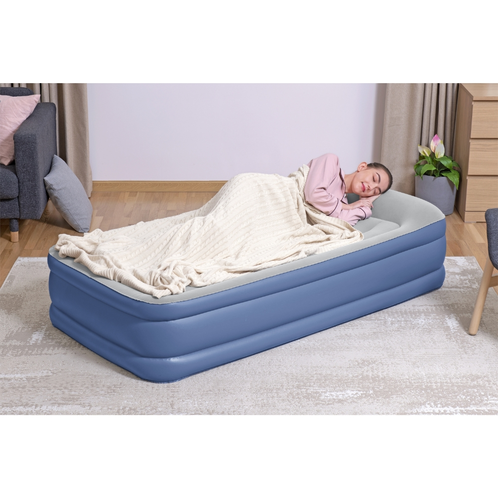 Femme dormant sur matelas gonflable bleu, couverte, tapis gris, chambre à coucher.