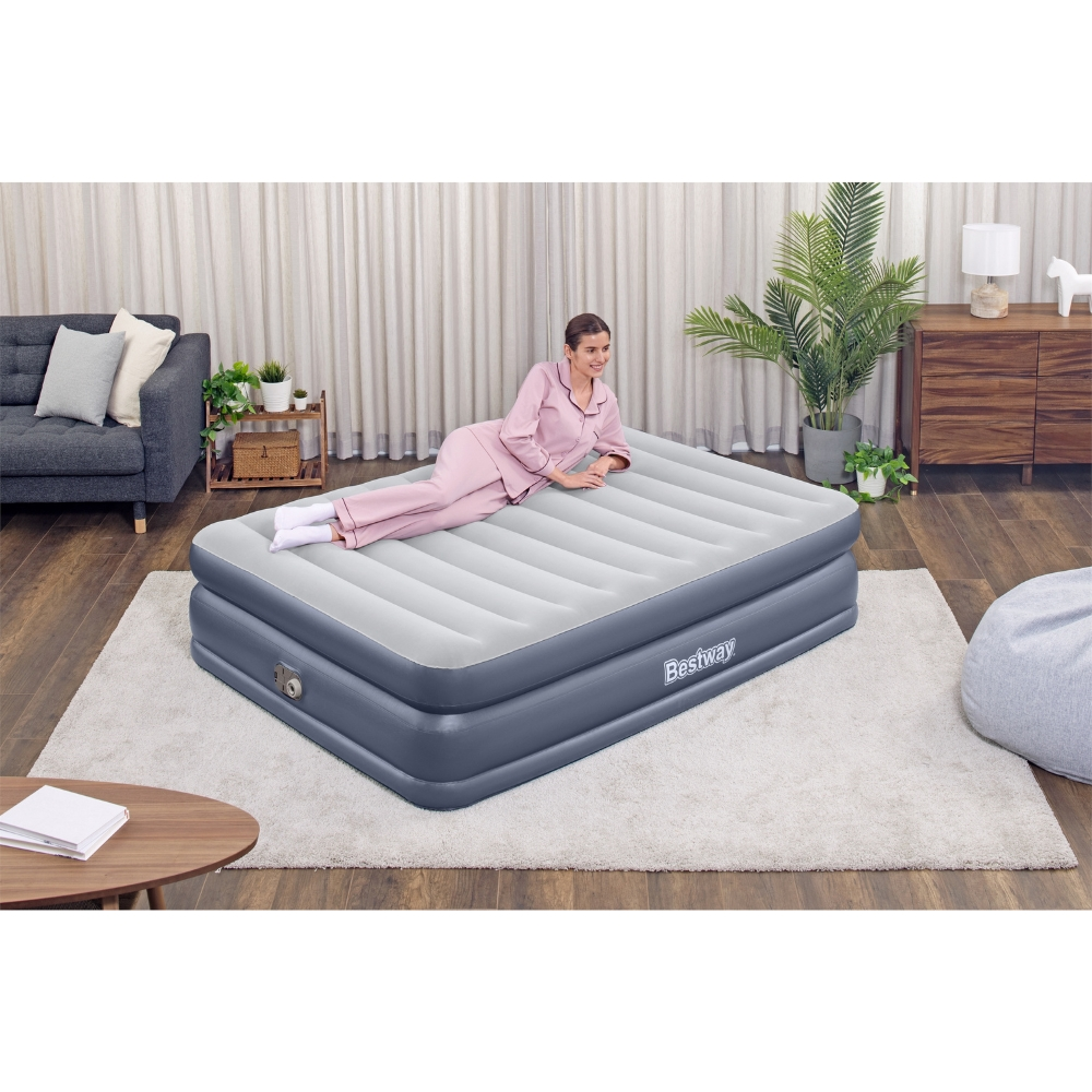 Vrouw liggend op een grijs en wit luchtmatras in een kamer. Interieur met kleed en gordijnen.