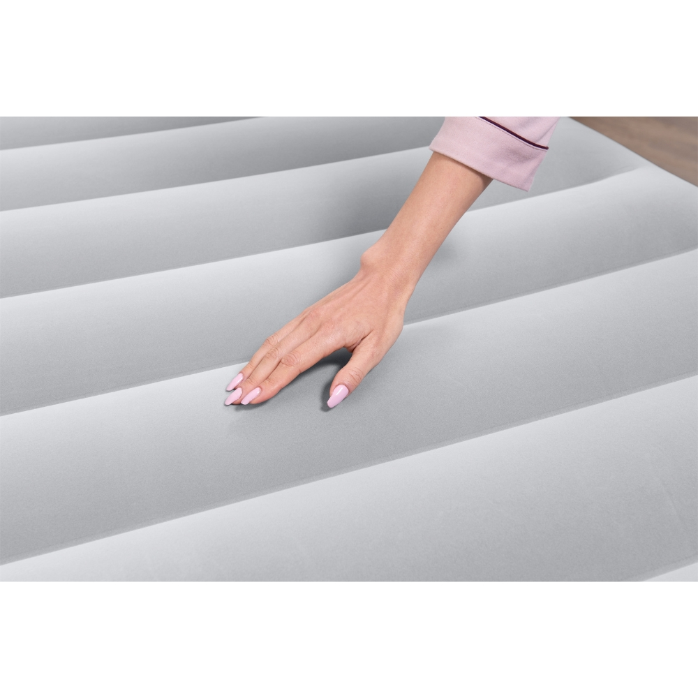 Close-up van een hand die een grijze opblaasbare matras aanraakt. De matras heeft horizontale lijnen.