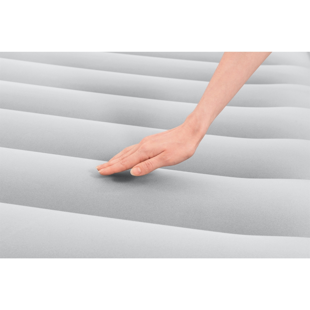 Une main touche doucement une surface de matelas gonflable gris. Le matelas a des crêtes parallèles.