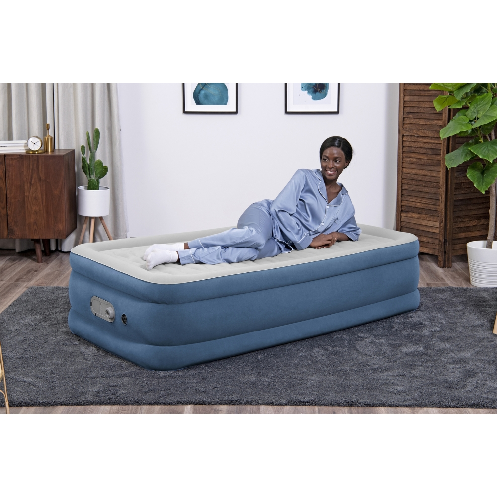 Een vrouw in een blauwe pyjama ligt op een blauw luchtmatras. Ze glimlacht.