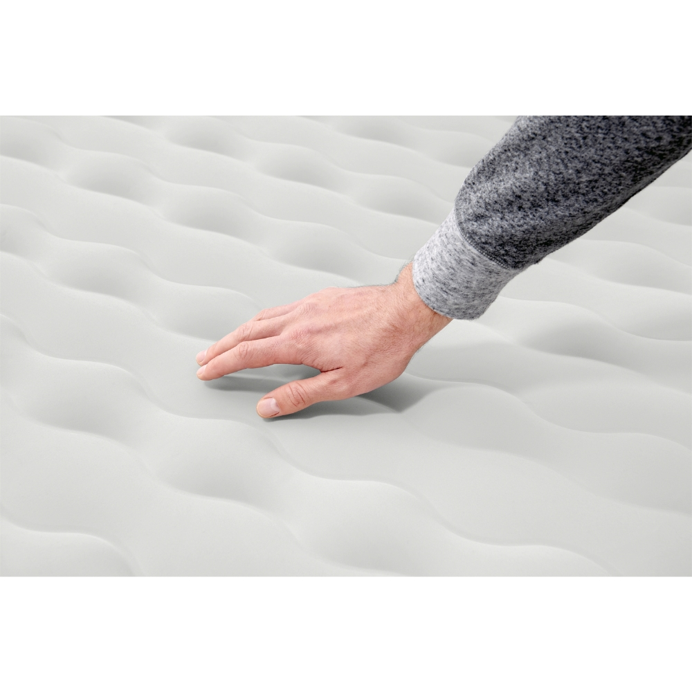 Une main repose sur un matelas pneumatique blanc. Le matelas a un design en forme de vague.
