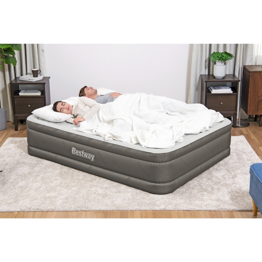 Un couple dort sur un matelas pneumatique gris. Ils sont couverts d'une couverture blanche.