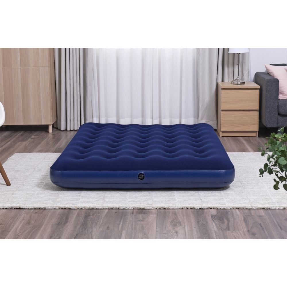 Een marineblauw luchtmatras ligt op een wit tapijt, met een witte muur en armaturen op de achtergrond.