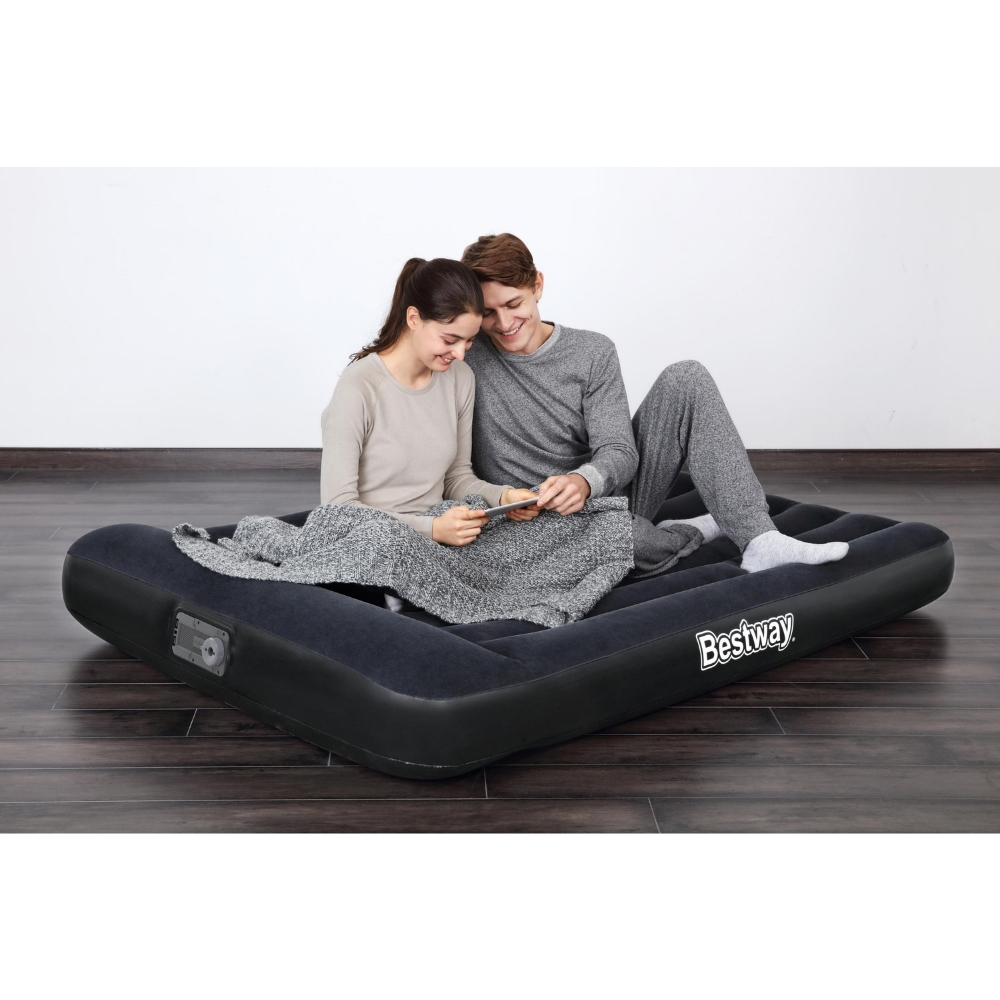 Couple assis sur un matelas gonflable noir Bestway. Ils regardent une tablette. Sol en bois sombre.