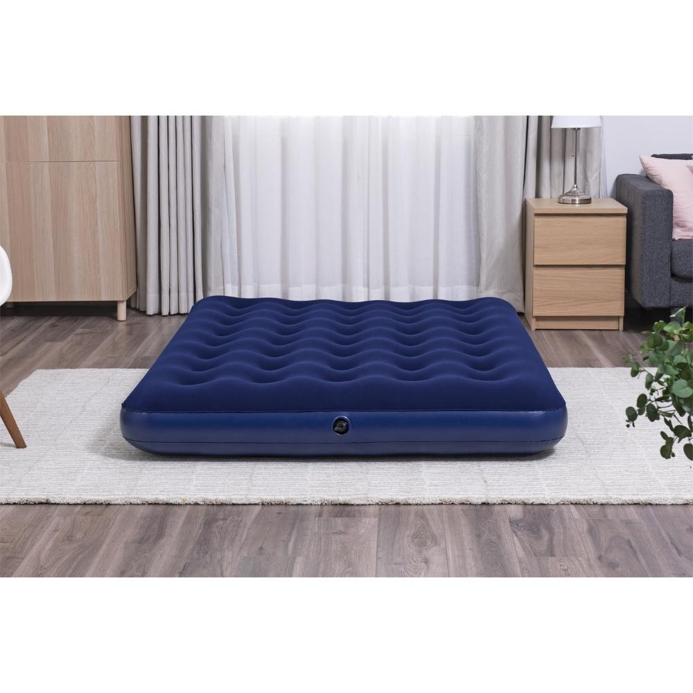 Donkerblauw opblaasbaar bed op een kleed. Houten kast en gordijnen op de achtergrond.