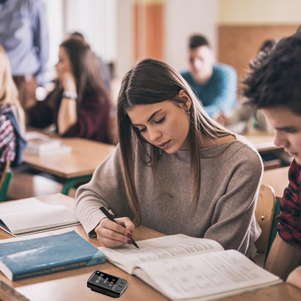 Uczeń pisze w notatniku przy biurku w klasie. Inni uczniowie są w tle.