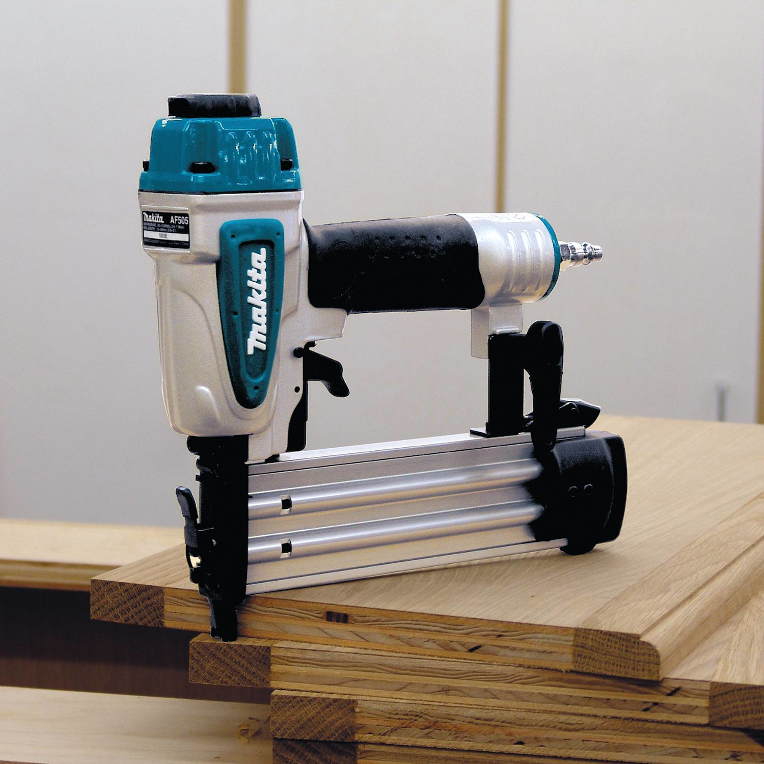 Una chiodatrice Makita AF506 su legno. È verde acqua, grigio e nero. Lo sfondo è bianco.
