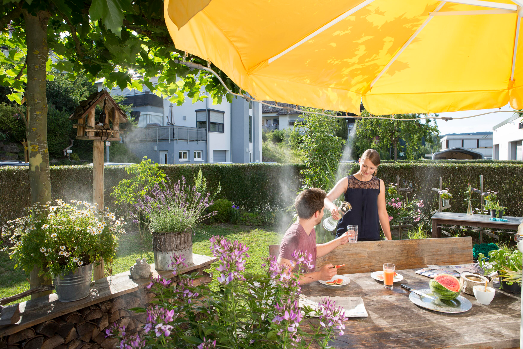 Paar genießt Essen und Trinken in einem Garten. Gelber Schirm im Hintergrund.