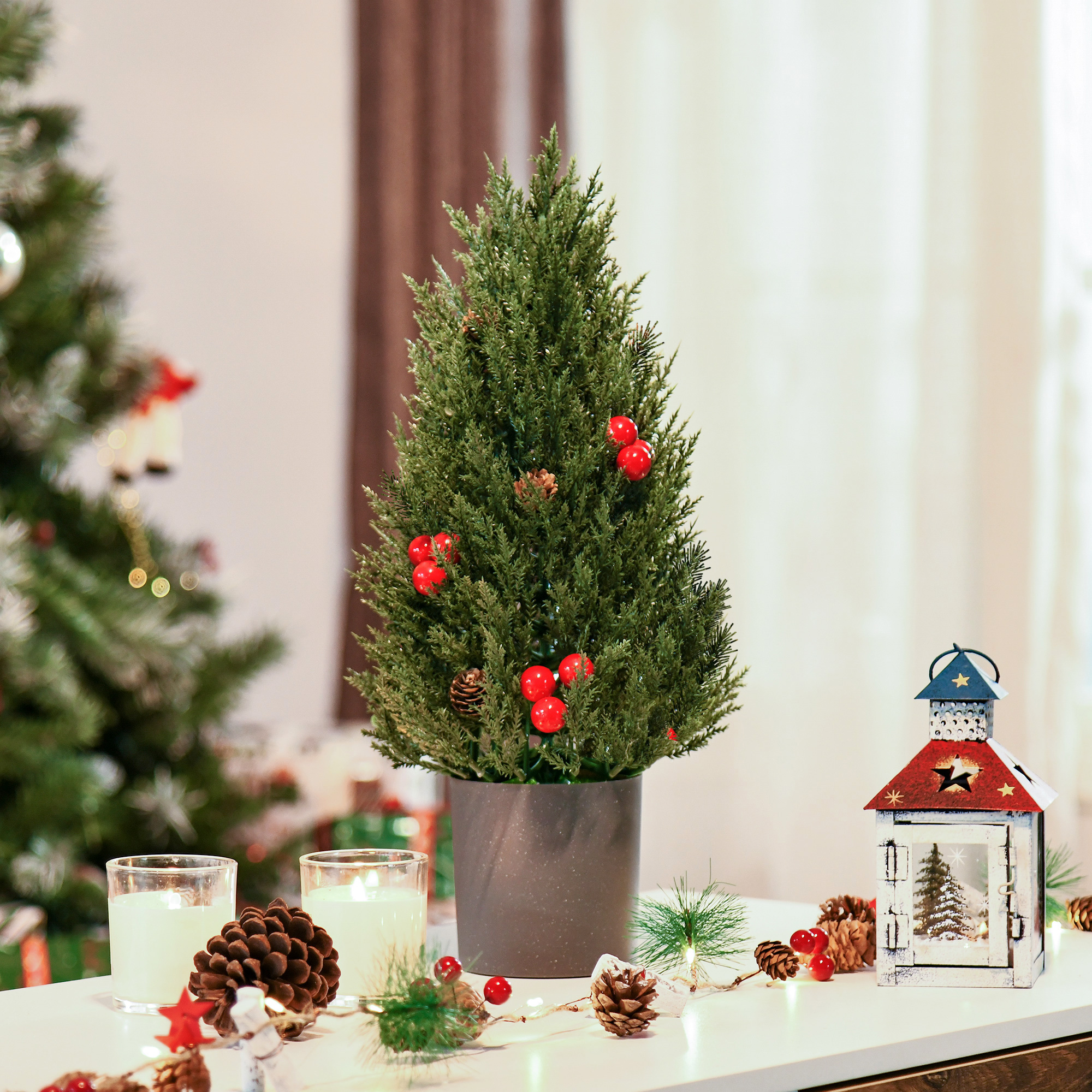 Kleiner Weihnachtsbaum in einem Topf, dekoriert mit roten Beeren, Kerzen und Lichtern.