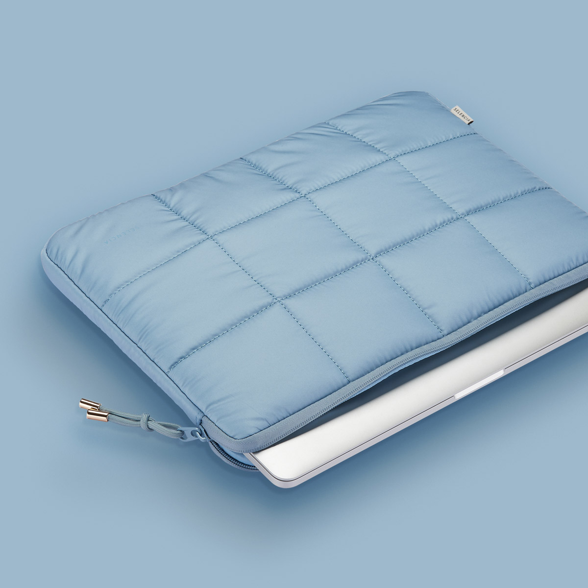Een blauwe gewatteerde laptoptas met een rits en een zilveren laptop erin.